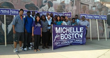 Standing above the first two letters of her name on the campaign banner, At-Large City Council candidate Michelle Wu joins supporters in Dudley Square.