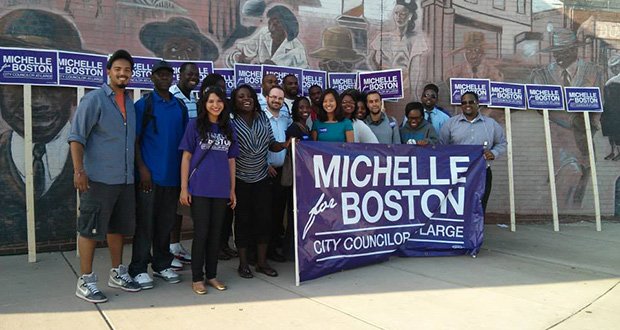 Standing above the first two letters of her name on the campaign banner, At-Large City Council candidate Michelle Wu joins supporters in Dudley Square.