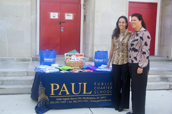 Takita Mason (left), Paul PCS director of development with Nina Albert, Walmart's director of community affairs on Monday, July 28 stand at the table displaying donated classroom supplies in front of the charter school in Northwest.