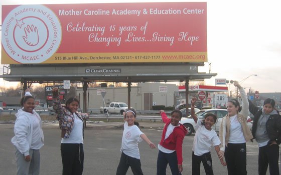 A group of students pose in front of the Mother Caroline Academy and Educational Center billboard, originally placed... A group of students pose in front of the Mother Caroline Academy and Educational Center billboard, originally placed...