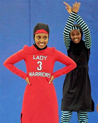 In this June 16, 2015 photo, Zubeda Chaffe, left, waits to get back into basketball practice in her new Lady Warriors uniform in Minneapolis. The girls came up with their own culturally sensitive sportswear designs that cover their arms, legs, hair and neck preserving the modesty their religion requires. One is a bright red uniform for the Lady Warriors and the other is a teal-and-black uniform with stripes _ good for all sports including swimming.