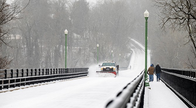 A snow plow clears the Nickel Bridge as two pedestrians walk the span on Feb. 19. The bridge was closed due to the winter weather.