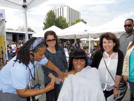 Public health nurse Deanna Bressler-Montgomery gives Tdap immunization to Compton Mayor Aja Brown at the city’s Back-to-School Family Health Fair on Aug. 2. The event, co-sponsored by South Los Angeles Health Projects and the Immunize L.A. Families Coalition, was held at the Compton Town Center. Looking on are Soledad Ramirez, member of the Immunize L.A. Families Coalition, and Heidi Kent, executive director, South L.A. Health Projects. Brown decided to become immunized after Oliver Brooks, M.D., chair of the Immunize L.A. Families Coalition, encouraged her to protect herself and those around her.