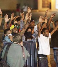 Protesters of the shooting death of Michael Brown Jr. take the “hands up, don’t shoot” stance in Ferguson, Mo. as police point their weapons at them.