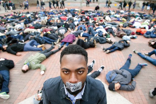 University of Michigan student William Royster stands with the “#Black Lives Matter” message taped over his mouth as he is surrounded by students at the Ann Arbor, Mich., university staging a recent “die-in” protesting the killing of unarmed black men by white police officers.