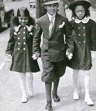Fashionably conscious children walk down the streets of Harlem, dressed to the nines, during the Harlem Renaissance era.