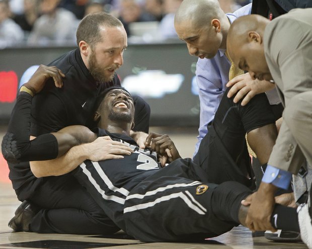 Virginia Commonwealth University basketball star Briante Weber grimaces as coach Shaka Smart, second from right, and others assist him moments after his injury during Saturday’s game against the University of Richmond at the Siegel Center.