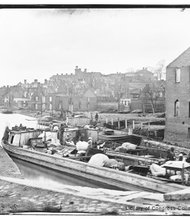 Newly liberated black people with all they own are packed onto a boat on Richmond’s Kanawha Canal as the charred ruins of the city stand in the background in this photograph, circa April-June 1865.