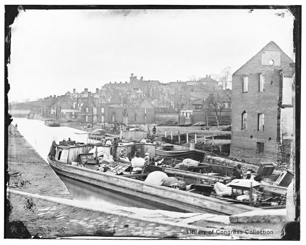 Newly liberated black people with all they own are packed onto a boat on Richmond’s Kanawha Canal as the charred ruins of the city stand in the background in this photograph, circa April-June 1865.