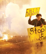 Tear gas clouds surround a woman demonstrating Tuesday night in Baltimore over the death of Freddie Gray, who died of severe injuries suffered while in police custody. Police fired the tear gas as part of efforts to prevent further violence. Rioting Monday night resulted in cars and buildings torched and businesses looted.  