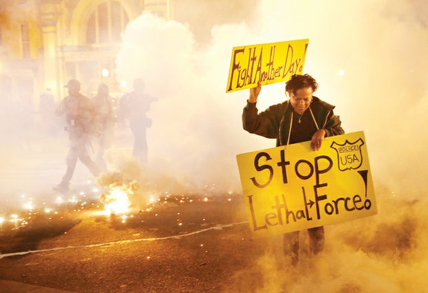 Tear gas clouds surround a woman demonstrating Tuesday night in Baltimore over the death of Freddie Gray, who died of severe injuries suffered while in police custody. Police fired the tear gas as part of efforts to prevent further violence. Rioting Monday night resulted in cars and buildings torched and businesses looted.  