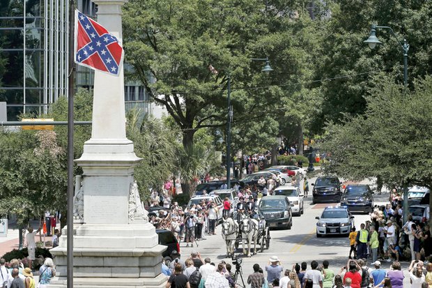 The Confederate battle flag, a symbol of racial hate, ironically waves Wednesday over the horse-drawn carriage bearing the casket of beloved African-American minister and state Sen. Clementa C. Pinckney to the South Carolina State Capitol in Columbia, where he will lie in state. 