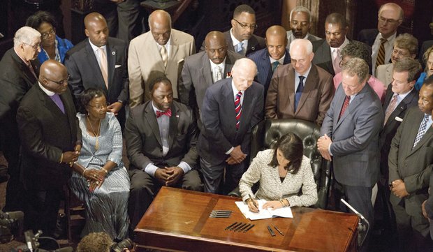 South Carolina Gov. Nikki Haley signs legislation July 9 permanently removing the Confederate flag from the State Capitol grounds in Columbia. She used nine pens that later were given to the families of the nine people killed by a white supremacist at Emanuel African Methodist Episcopal Church in Charleston.