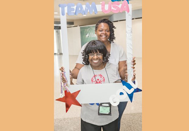 
Mary Davis, front, enjoys an Olympic hero’s welcome Monday night when she arrives home at Richmond International Airport. Among the bevy of family and friends greeting her was counselor Keisha Walker. Left, friends hold a sign to show their pride in Team Virginia’s medal-winning efforts.