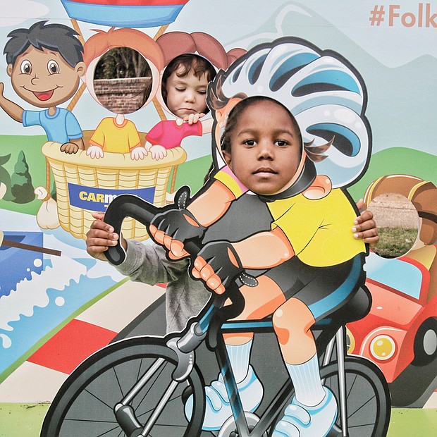 Raching Towards fun - Marcus McDowell, front, inserts his face into the image of a bicyclist on a cutout Saturday at the 11th Annual Richmond Folk Festival along the banks of the James River in Downtown. More than 40 music artists and groups were featured at the free outdoor three-day event that drew a crowed estimated at 200,000. 