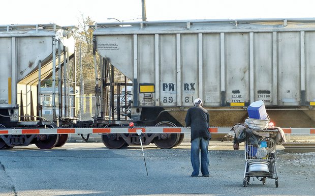 A patient pedestrian waits to push his cart filled with metal and other items across the railroad tracks. He is on his way to turn his collection into cash at the recycling plant at Stratton Metals, 900 Brook Road, on North Side. He is among hundreds in Richmond who make money collecting paper, aluminum cans and other recyclables.