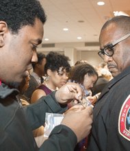 Twenty-two new firefighters will begin serving in stations throughout the city. Kevon Young, left, pins a badge on his father, new Firefighter Keith Young, during the ceremony. 