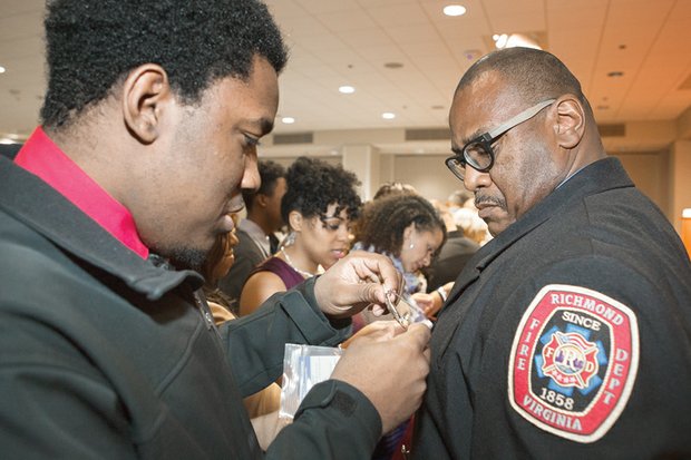 Twenty-two new firefighters will begin serving in stations throughout the city. Kevon Young, left, pins a badge on his father, new Firefighter Keith Young, during the ceremony. 