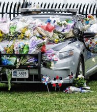 Honoring slain trooper //
Angela Courteau and her daughters, Elara, 5, and Nina, 1, place flowers on the car of slain Virginia State Police Trooper Chad P. Dermyer last Friday at State Police headquarters in Chesterfield County. People from Metro Richmond and around the state and nation paid their respects to the 37-year-old Michigan native who was fatally shot during a counterterrorism training exercise last Thursday at the Richmond Greyhound bus station. Authorities said other troopers inside the bus station then shot and killed the gunman, James Brown III of Aurora, Ill. Two women were wounded, including an athlete from the University of Binghamton in New York who was headed to a track and field event in Williamsburg. They were hospitalized with injuries described as not life threatening. Gov. Terry McAuliffe and police officers from 20 states were among the thousands of mourners at Trooper Dermyer’s funeral Tuesday in Hampton. He was buried in Gloucester County.