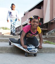 Carefree //
As her friend looks on, Shaniy Smith, 6, maneuvers her skateboard down steps along a walkway in Richmond’s Gilpin Court as they joyfully played Monday in the sunshine. In the background, Richmond Police Chief Alfred Durham and other officers walk through the public housing community meeting with neighbors to talk about their safety concerns. They later convened at the Calhoun Community Center to talk about a sudden spike in major crimes, especially gun violence, this year. Chief Durham conducted a similar walk Tuesday in the Randolph community.