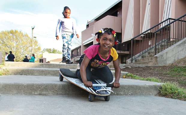 Carefree //
As her friend looks on, Shaniy Smith, 6, maneuvers her skateboard down steps along a walkway in Richmond’s Gilpin Court as they joyfully played Monday in the sunshine. In the background, Richmond Police Chief Alfred Durham and other officers walk through the public housing community meeting with neighbors to talk about their safety concerns. They later convened at the Calhoun Community Center to talk about a sudden spike in major crimes, especially gun violence, this year. Chief Durham conducted a similar walk Tuesday in the Randolph community.