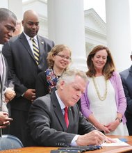Gov. McAuliffe signs the sweeping order restoring felons’ voting rights Friday as supporters watch. Among them, from left: former Secretary of the Commonwealth Levar Stoney, Henrico Delegate Lamont Bagby, current Secretary of the Commonwealth Kelly Thomasson, First Lady Dorothy McAuliffe and Chesapeake Delegate Lionell Spruill Sr. Location: South Portico of the State Capitol.