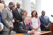 Gov. McAuliffe signs the sweeping order restoring felons’ voting rights Friday as supporters watch. Among them, from left: former Secretary of the Commonwealth Levar Stoney, Henrico Delegate Lamont Bagby, current Secretary of the Commonwealth Kelly Thomasson, First Lady Dorothy McAuliffe and Chesapeake Delegate Lionell Spruill Sr. Location: South Portico of the State Capitol.