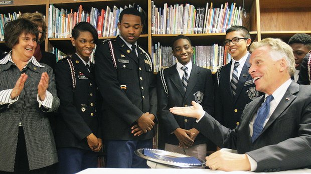 Special delivery //
Cameras flash as Sgt. Robot, left, built by students at Richmond’s Franklin Military Academy, delivers House Bill 831 to a delighted and impressed Gov. Terry McAuliffe, above, at a signing ceremony Monday at the high school in Church Hill. Gov. McAuliffe praised the public military school’s students for the technology demonstration before signing into law legislation elevating computer science to equal status with English, math, science and history in the state’s Standards of Learning. Joining in applauding the students is state Secretary of Education Anne B. Holton, left. Last week, the governor signed a separate bill that puts vocational, career and technical education on par with academics as part of an overhaul of high school learning beginning in 2018.