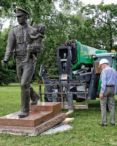 A heavy-duty forklift positions the statue on its new concrete base facing Blanton Avenue at Trafford Road. Retired Richmond police officer Glenwood W. Burley, wearing a hard hat, began a campaign to relocate the statue in May 2015 to ensure it would be properly tended and more visible to the public. Sculptor Maria Kirby-Smith created the statue of an officer holding a child that was dedicated in 1987.