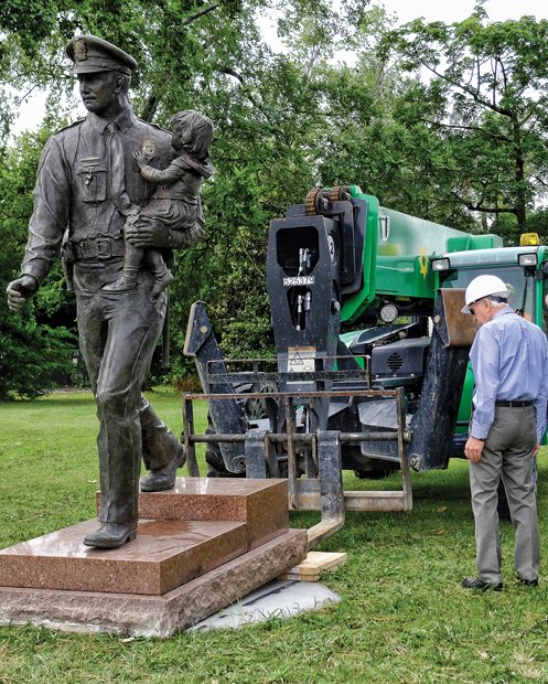 A heavy-duty forklift positions the statue on its new concrete base facing Blanton Avenue at Trafford Road. Retired Richmond police officer Glenwood W. Burley, wearing a hard hat, began a campaign to relocate the statue in May 2015 to ensure it would be properly tended and more visible to the public. Sculptor Maria Kirby-Smith created the statue of an officer holding a child that was dedicated in 1987.