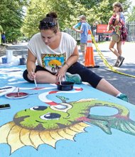 Abby Klein creates a work of art Friday atop a storm drain on Tredegar Street near Brown’s Island as curious passers-by watch her progress. She is one of five artists selected by the Richmond Department of Public Utilities from 55 for the first phase of the Storm Drain Art Project. Ms. Klein’s work is titled, “You drop it, I drink it.” The other four artists who are painting drains along Tredegar Street are Alfonso Perez Acosta, Nicole Gomez, Melissa Greedy and Richard Lucente. 
The city is paying a commission of $300 to each artist and later plans to award a $200 prize to the artist whose work the public votes as their favorite. The project was set up as a fun, creative approach to educate the public to keep the drains free of litter and not use the drains to get rid of oil and other toxins that could pollute the city’s waterways and, ultimately, the James River into which storm water flows. 