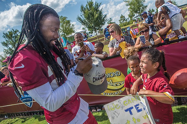 Big thanks  for big fans //  The Washington NFL team wrapped up its Richmond training camp Sunday, but not before hosting its traditional Fan Appreciation Day last Saturday.
With the line of fans wrapped around West Leigh Street, the Bon Secours training center was mobbed with autograph seekers of all ages.
Cornerback Greg Toler, left, a graduate of the former St. Paul’s College in Lawrenceville, signs a hat for Aniya Neeson,