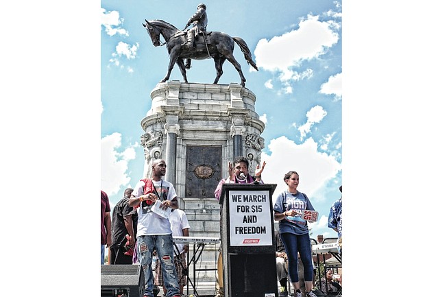 Dr. William Barber II, left, president of the North Carolina NAACP, energizes the crowd of thousands who withstood Saturday’s scorching heat to march from Monroe Park to the Monument Avenue statue of Confederate Gen. Robert E. Lee to call for an end to slave wages. 