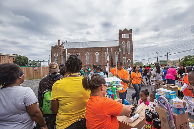 Sixth Mount Zion Pastor Tyrone Nelson, center, adds household items to an array of goods, clothing and food
that were given away last Sunday by the congregation in Jackson Ward.