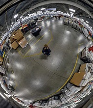 Employees work among a maze of conveyor belts and sorting machines in the huge building that is the size of 12 football fields and handles mail from Central and Eastern Virginia. Left, Free Press photographer Sandra Sellars seeks to give a sense of the building’s size by photographing a portion of the center reflected in a ceiling mirror. 