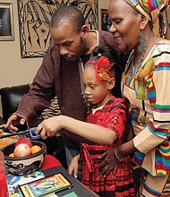 Sakara Bey, 8, lights the Kwanzaa kinara with her father, Hakim Bey, and grandmother, Shakila Davis, on Wednesday at Mrs. Davis’ Henrico County home. The family is celebrating the third day of Kwanzaa, ujima, or collective work and responsibility. 