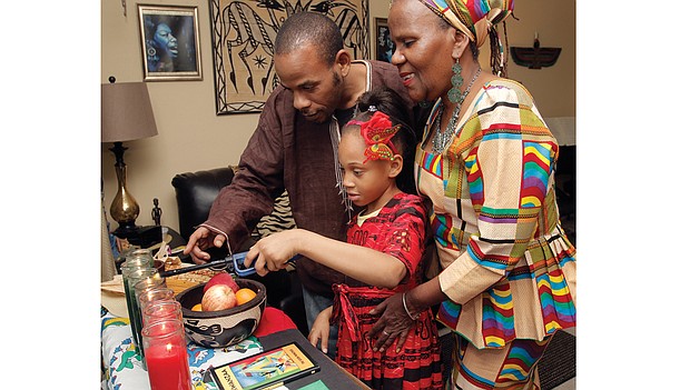 Sakara Bey, 8, lights the Kwanzaa kinara with her father, Hakim Bey, and grandmother, Shakila Davis, on Wednesday at Mrs. Davis’ Henrico County home. The family is celebrating the third day of Kwanzaa, ujima, or collective work and responsibility. 