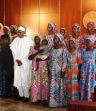 Nigerian President Muhammadu Buhari (C) poses on October 19, 2016 with the 21 Chibok girls who were released by Boko Haram last week, at the State House in Abuja, Nigeria. Speaking at the presidential villa in Nigeria’s capital of Abuja, Buhari addressed the girls and their families saying ‘we shall redouble efforts to ensure that we fulfil our pledge of bringing the remaining girls back home’. (AFP/Philip OJISUA)