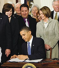 Surrounded by members of the U.S. House of Representatives and Senate, President Obama signs the Affordable Care Act in March 2010 as youngster Marcelas Owens of Seattle watches.