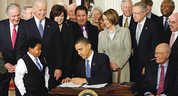 Surrounded by members of the U.S. House of Representatives and Senate, President Obama signs the Affordable Care Act in March 2010 as youngster Marcelas Owens of Seattle watches.