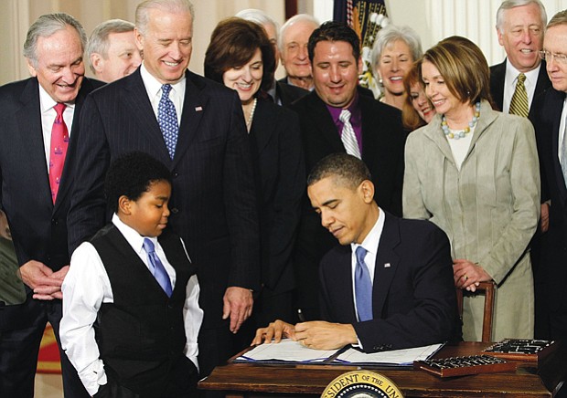 Surrounded by members of the U.S. House of Representatives and Senate, President Obama signs the Affordable Care Act in March 2010 as youngster Marcelas Owens of Seattle watches.