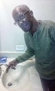 Ernest L. Fox uses his fingers to test the water temperature in his new apartment. He says water never gets hot enough to use for shaving or showering. 