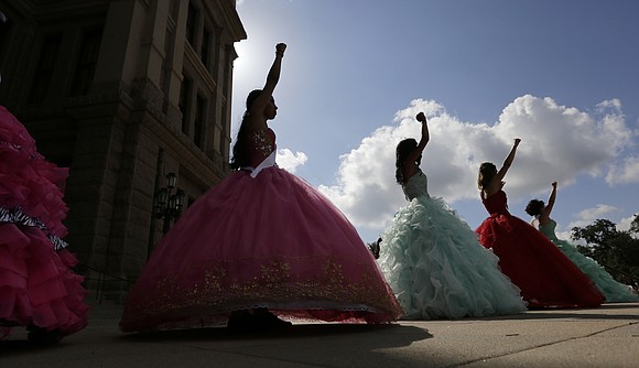 A group of 15 teenage girls, dressed in brightly colored gowns, stood in front of the Texas State Capitol to …
