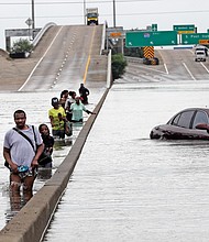 Evacuees wade down a flooded section of Interstate 610 as floodwaters rise Sunday in Houston.
