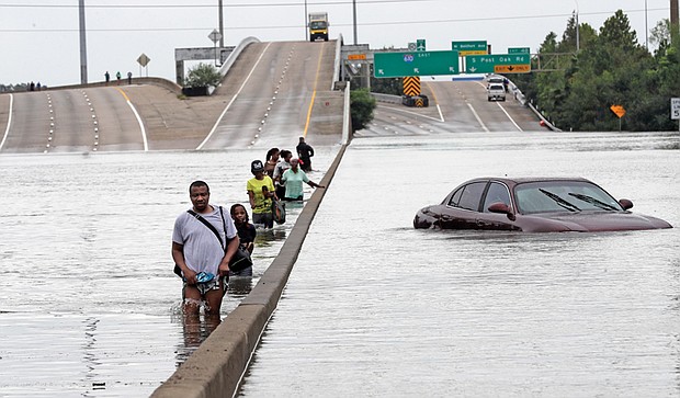 Evacuees wade down a flooded section of Interstate 610 as floodwaters rise Sunday in Houston.
