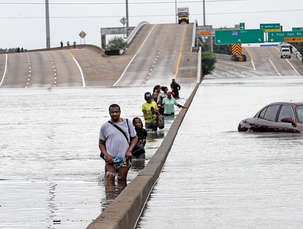Evacuees wade down a flooded section of Interstate 610 as floodwaters rise Sunday in Houston.
