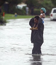 Charlie Riedel/ Associated Press
A man carries a child across a flooded street in Houston on Sunday as they search for higher ground.