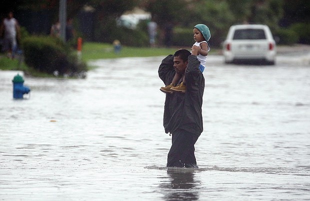 Charlie Riedel/ Associated Press
A man carries a child across a flooded street in Houston on Sunday as they search for higher ground.