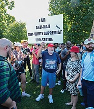 Counterprotesters surround Chris Willis, dressed in a T-shirt supporting President Trump and a cap bearing the Trump slogan “Make America Great Again,” as he holds up a sign supporting the Confederate statues.