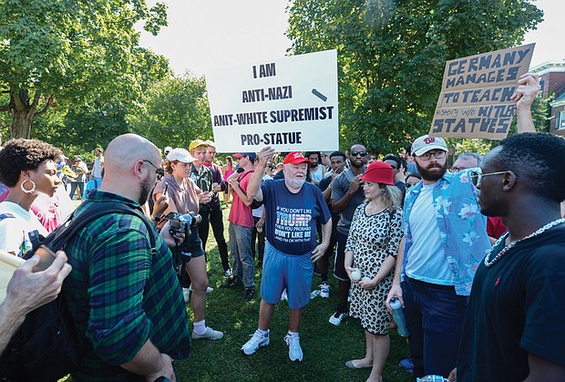 Counterprotesters surround Chris Willis, dressed in a T-shirt supporting President Trump and a cap bearing the Trump slogan “Make America Great Again,” as he holds up a sign supporting the Confederate statues.